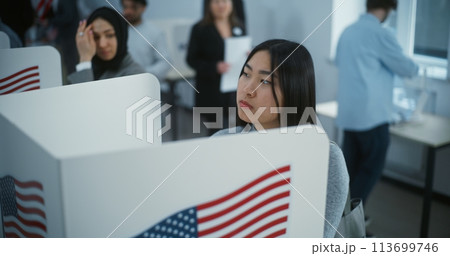 Asian female American citizen votes in booth in polling station 113699746