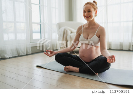 Pregnancy prenatal breathing. Pregnant woman with big belly sitting in lotus pose on yoga matt at home. Pregnant girl practicing yoga mindfulness meditation. Relaxation self care during pregnancy 113700191