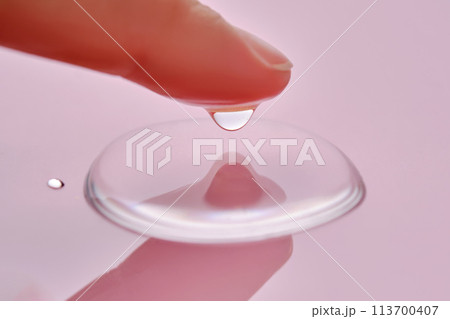 A finger touches a drop of cosmetic product on a pink background. A finger touches a drop of cosmetic product on a pink background. 113700407