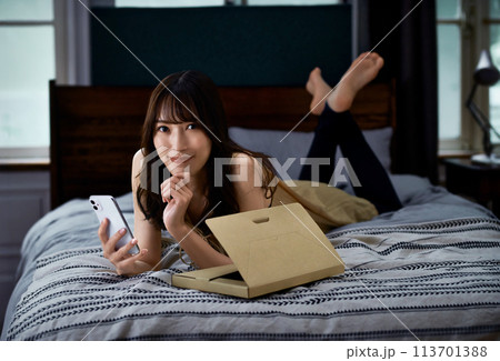 ヘッドでうつ伏せになりながらネットショッピングする若い女性 113701388