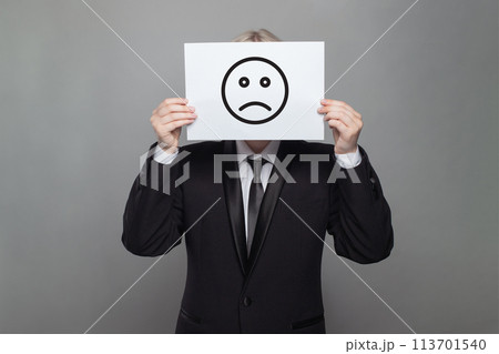 Portrait of Anonymous businessman hiding his head behind white paper with sad emoticon 113701540