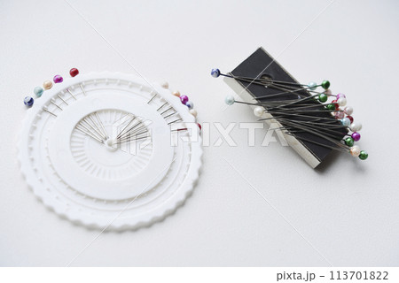 Multicolored pins on a white background. Pins and a sewing magnet. Multicolored pins on a white background. Pins and a sewing magnet. 113701822