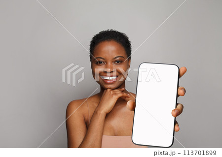 Cheerful healthy woman holding smartphone with white empty blank screen display on gray Cheerful healthy woman holding smartphone with white empty blank screen display on gray 113701899