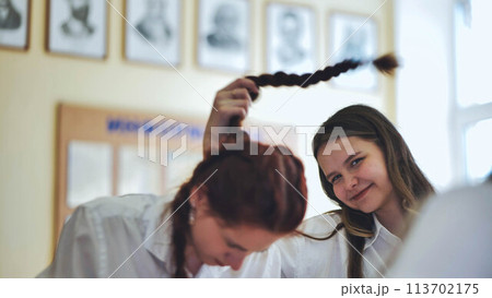 Fun schoolgirls in the classroom. Girl playing with her friend's pigtail. Fun schoolgirls in the classroom. Girl playing with her friend's pigtail. 113702175