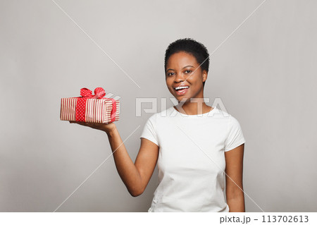 Happy excited woman in white t-shirt holding gift box surprise against white studio wall  113702613