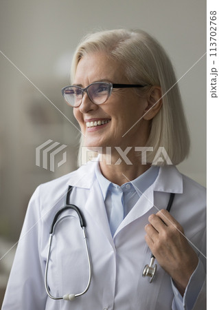 Happy mature female physician doctor in uniform posing indoor Happy mature female physician doctor in uniform posing indoor 113702768