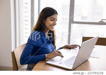 Happy focused Indian freelancer woman working at laptop at home Happy focused Indian freelancer woman working at laptop at home 113703238