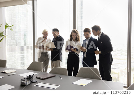 Focused colleagues working on project standing together in conference room Focused colleagues working on project standing together in conference room 113703239