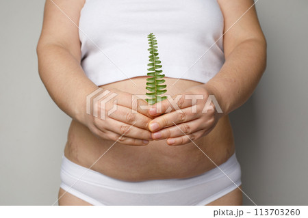 young adult human stomach tummy and green leaf in female hand closeup. 113703260
