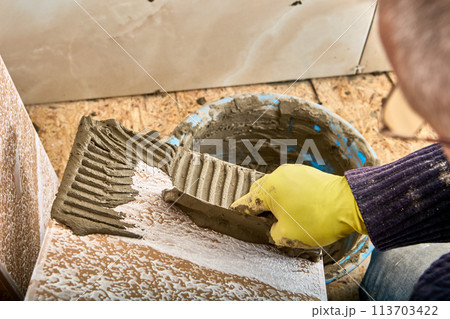 Tiler applies adhesive to tiles before installing them on wall. Tiler applies adhesive to tiles before installing them on wall. 113703422