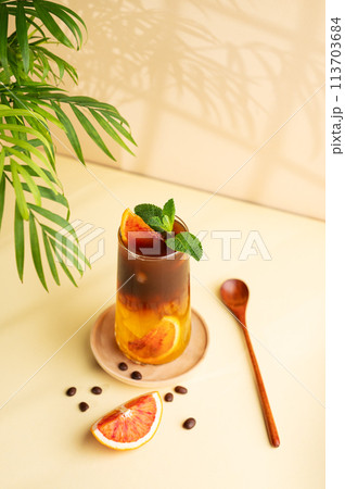 Americano coffee with orange juice (bumble) in a tall glass with ice and mint on a yellow background 113703684
