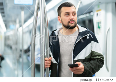 Portrait of european man standing in underground carriage and using phone 113708672