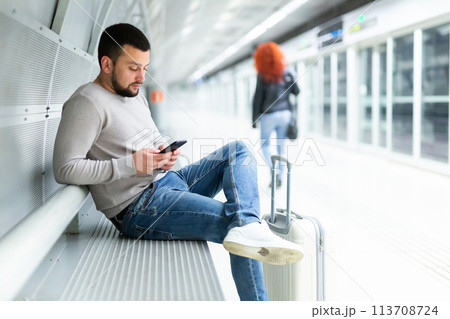 Bearded traveler with phone waiting for train on bench at metro station 113708724