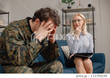 Soldier and psychiatrist sitting on couch during therapy session. Man wearing military uniform. Male warrior with ptds talking to psychiatrist. 113709240