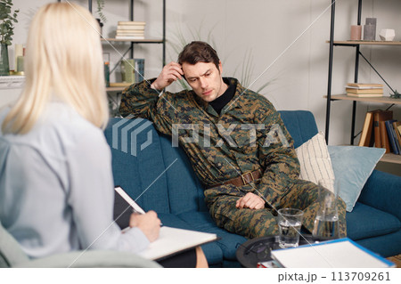 Soldier and psychiatrist sitting on couch during therapy session. Man wearing military uniform. Male warrior with ptds talking to psychiatrist. 113709261
