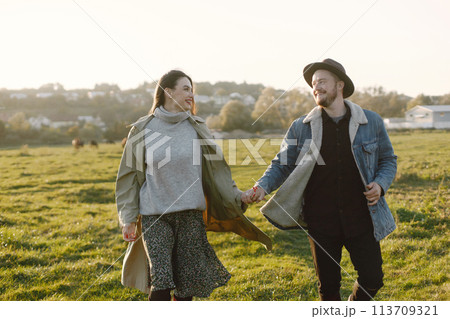 Man and woman in fashion clothes resting on a nature together. Man wearing jacket and a black hat and woman skirt and red boots. Photo of romantic couple outdoors. 113709321