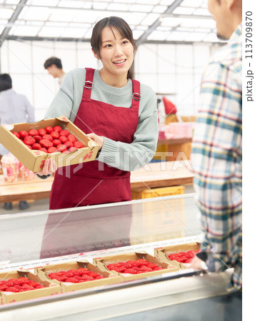 笑顔でイチゴを販売するエプロン姿の若い女性店員 113709870