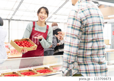 笑顔でイチゴを販売するエプロン姿の若い女性店員 113709873