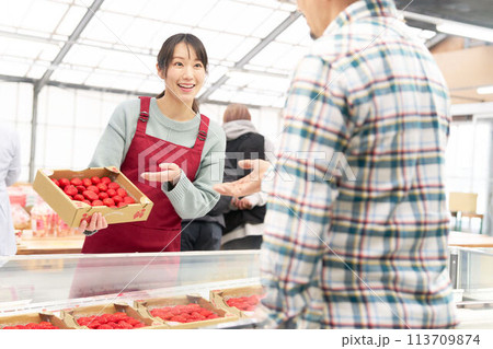 笑顔でイチゴを販売するエプロン姿の若い女性店員 113709874