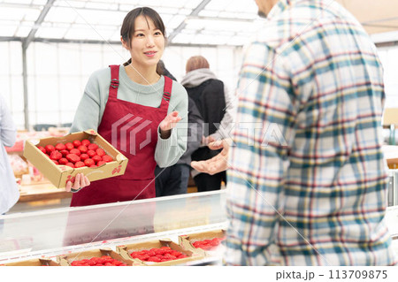 笑顔でイチゴを販売するエプロン姿の若い女性店員 113709875