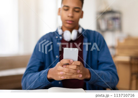 Focused black teen guy using phone with headphones around neck 113710716
