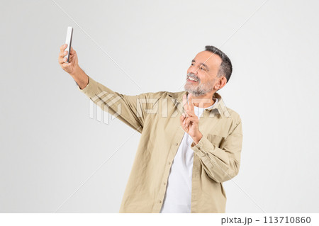 Mature man taking selfie with smartphone on white background 113710860
