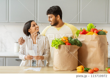 Indian couple analyzing grocery expenses with love Indian couple analyzing grocery expenses with love 113710972