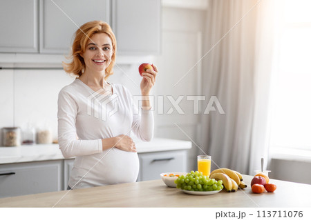 Pregnant lady holding apple in kitchen, copy space 113711076
