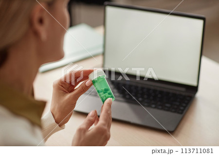 Close up of unrecognizable female doctor holding bottle of pills and talking to client online via laptop copy space 113711081
