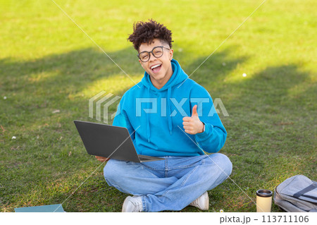 Cheerful student with laptop on grass, studying at park Cheerful student with laptop on grass, studying at park 113711106