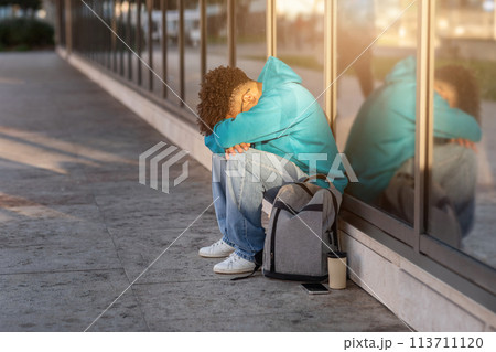Person sitting alone on sidewalk at sunset 113711120