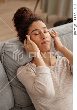 Vertical high angle portrait of young woman enjoying self care at home and doing face massage Vertical high angle portrait of young woman enjoying self care at home and doing face massage 113711153