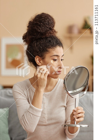 Vertical side view portrait of young woman applying moisturizing patches and looking in mirror at home Vertical side view portrait of young woman applying moisturizing patches and looking in mirror at home 113711161