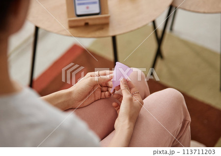 Top view closeup of female hand holding pink menstrual cup sitting on couch at home copy space 113711203