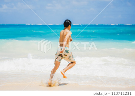 ハワイの砂浜でターコイズブルーの海に向かって走る水着姿の若い男性 ハワイの砂浜でターコイズブルーの海に向かって走る水着姿の若い男性 113711231