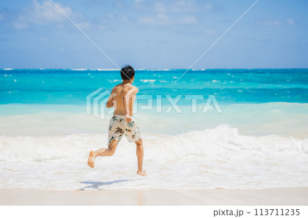 ハワイの砂浜でターコイズブルーの海に向かって走る水着姿の若い男性 113711235