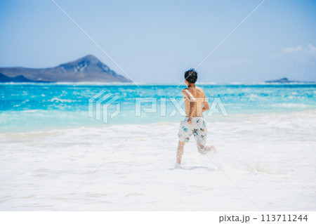 ハワイの砂浜でターコイズブルーの海に向かって走る水着姿の若い男性 113711244
