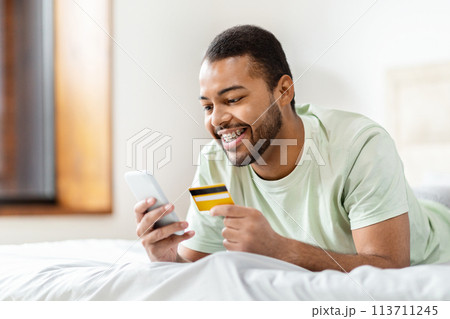 Blck man looking at phone while holding credit card 113711245