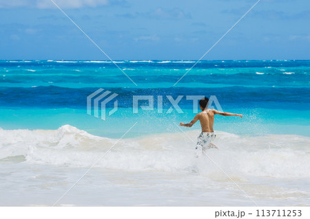 ハワイの砂浜でターコイズブルーの海に向かって走る水着姿の若い男性 113711253