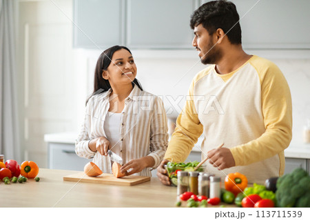 Indian Spouses Having Conversation While Preparing Food In Cozy Kitchen 113711539