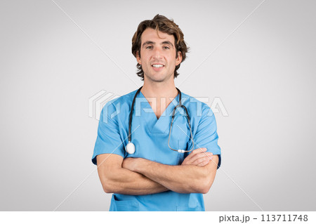 Confident male nurse in blue scrubs with arms crossed and stethoscope 113711748