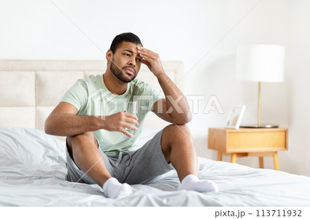 Man sitting on bed with glass of water 113711932