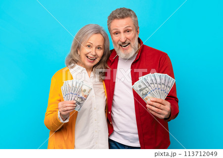 senior man and woman holding money cash against blue backdrop senior man and woman holding money cash against blue backdrop 113712049
