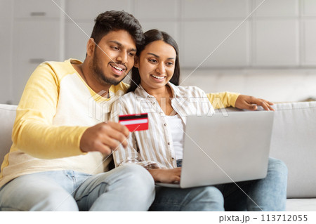 Millennial couple holding card and laptop at home Millennial couple holding card and laptop at home 113712055