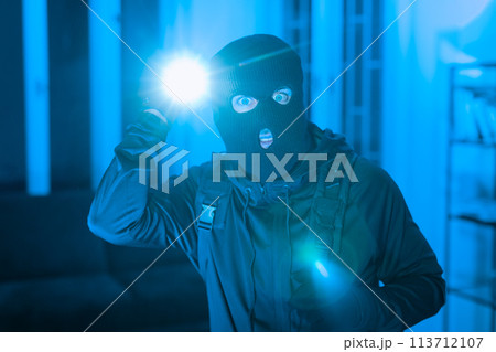 Burglar with flashlight in a dark room 113712107