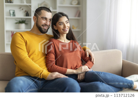 Couple sitting closely on their couch Couple sitting closely on their couch 113712126