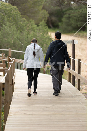 A man and woman are walking on a wooden bridge - rear view 113712139