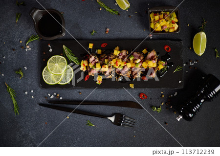 Sliced Organic grilled Tuna fillet covered with sesame seeds and mango salsa on black stone serving board 113712239
