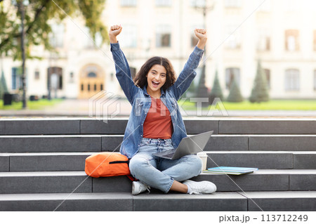 Excited student with laptop on campus steps Excited student with laptop on campus steps 113712249