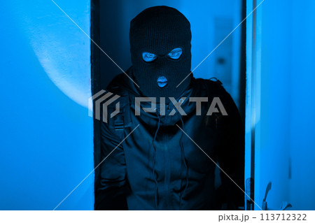 Mysterious figure of man in blue-lit apartment corridor 113712322